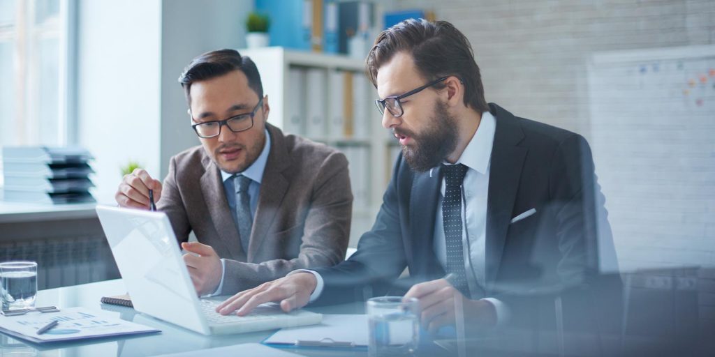Two business consultants discussing documents at a laptop